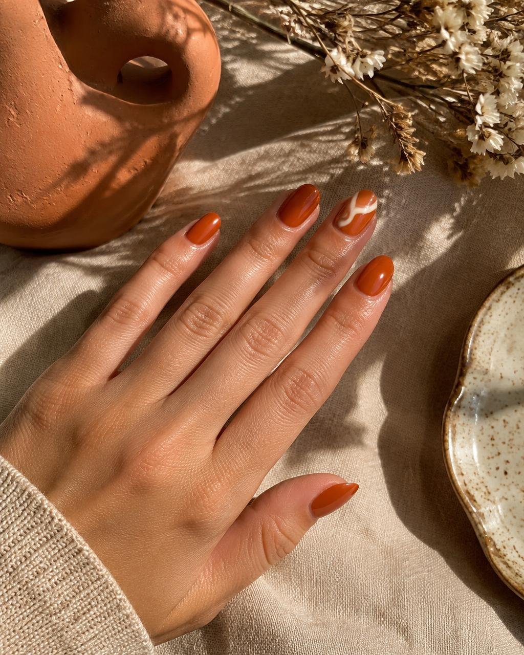 Burnt orange almond nails with a cream curved accent on linen