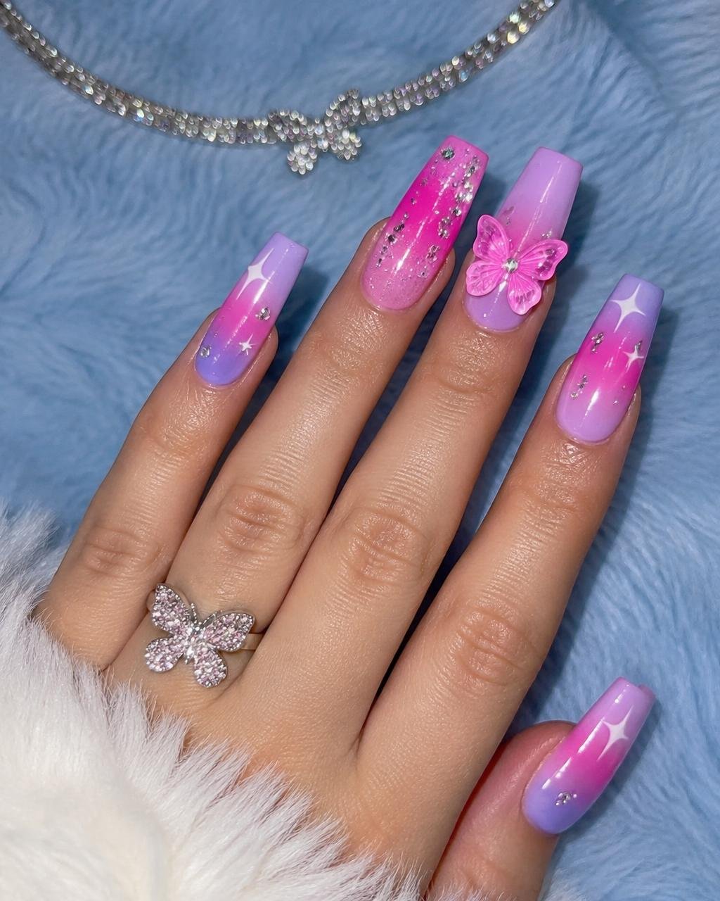 Pink and lilac airbrush coffin nails with stars and a 3D butterfly charm on baby blue fur